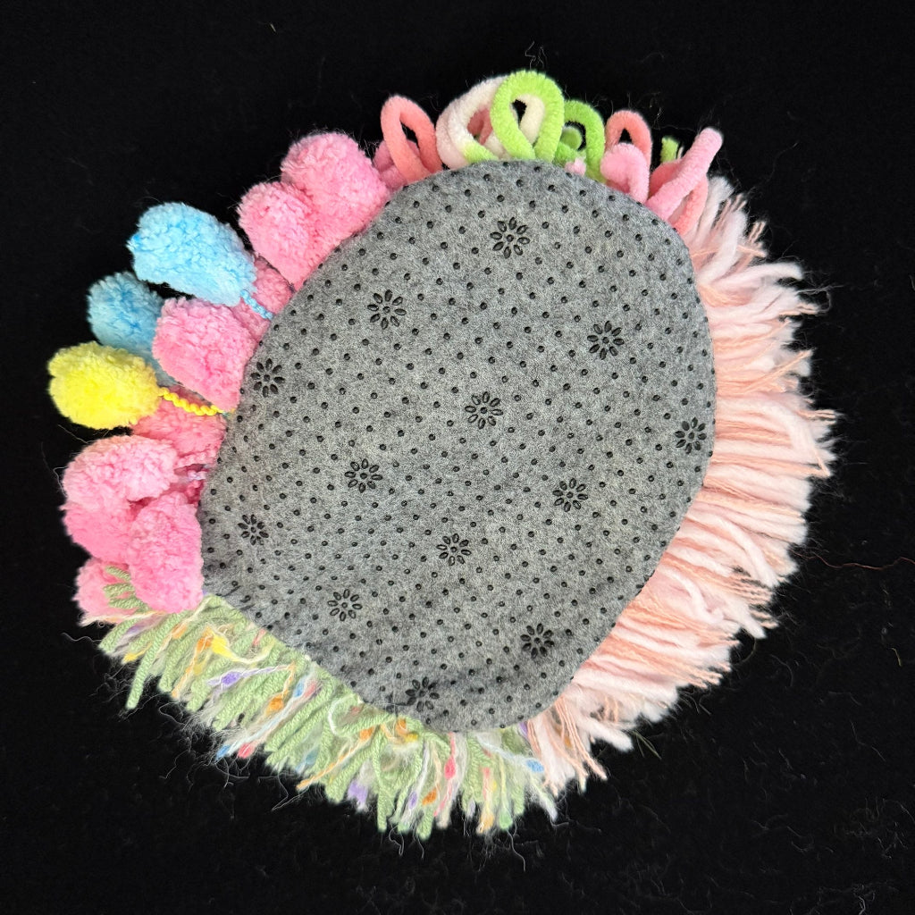 Handmade Blossom Puddle pastel pom-pom crochet coaster back view showing grey non-slip floral pattern base with colorful pom-pom and fringe border on black background – Sylva Garden