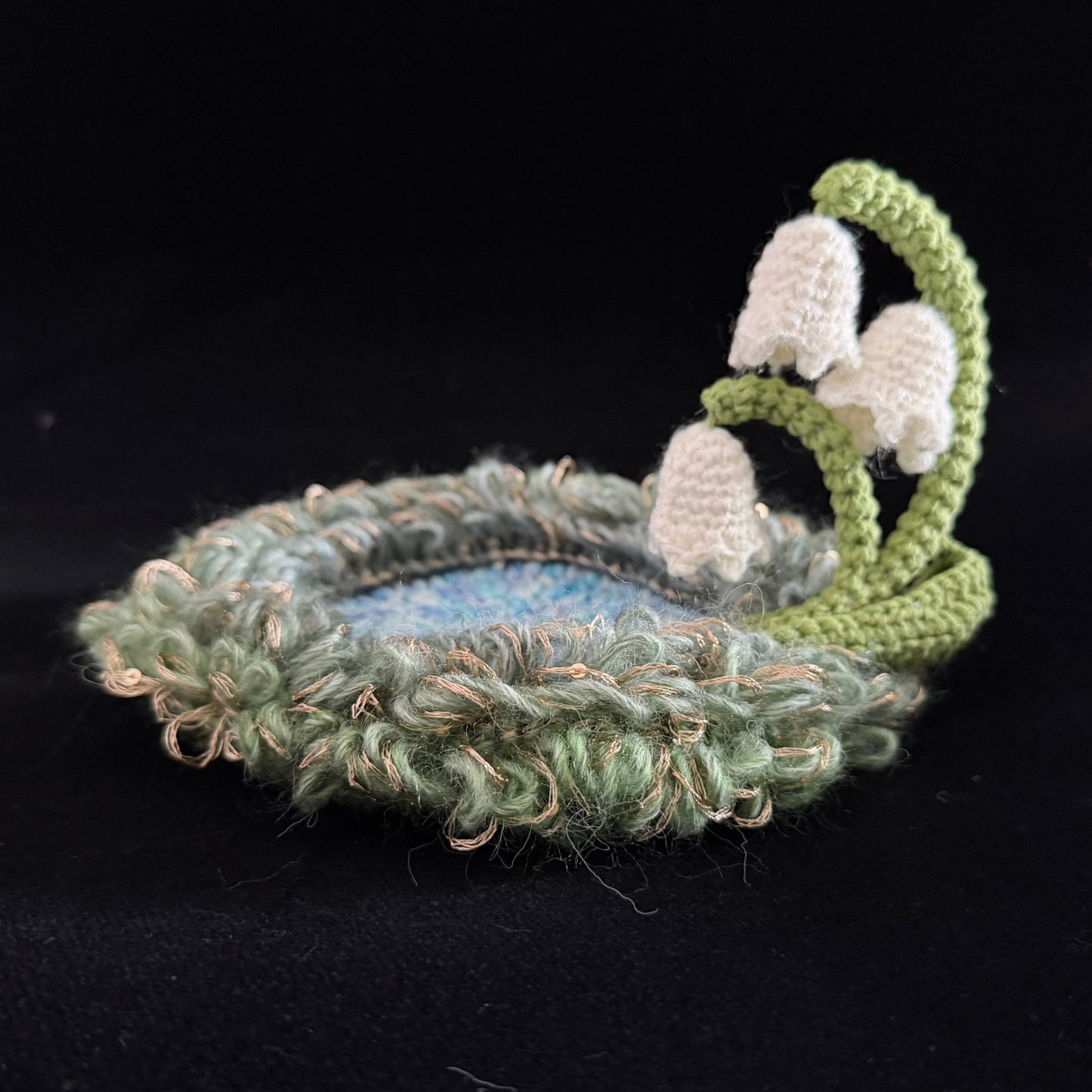 Handmade Dewbell lily of the valley crochet moss coaster side view showing layered green moss texture and white bell bloom stem on black background – Sylva Garden