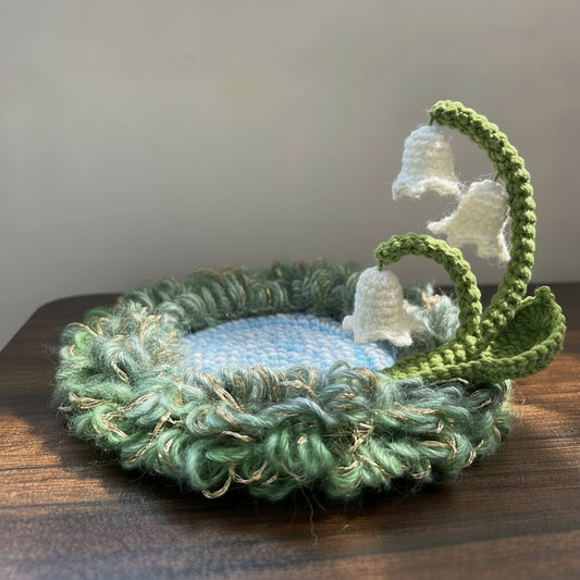 Handmade Dewbell lily of the valley crochet moss coaster with white bell blooms and green stem on wooden table, side view – Sylva Garden