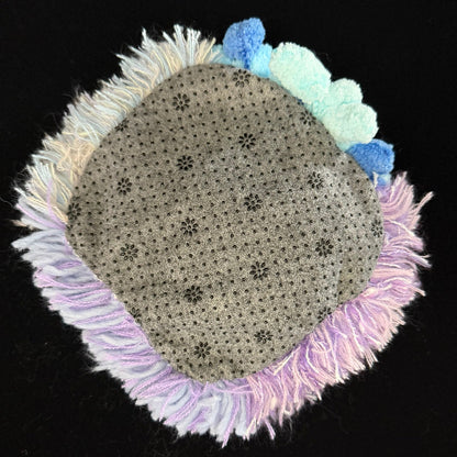 Handmade Dreamy Bog lavender blue pink coral pom-pom crochet coaster back view showing beige floral non-slip fabric base with lavender and pink fringe border on black background – Sylva Garden