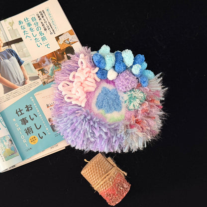 Handmade Dreamy Bog lavender blue pink coral pom-pom crochet coaster styled with Japanese magazine and beeswax candle on black background, overhead lifestyle view – Sylva Garden