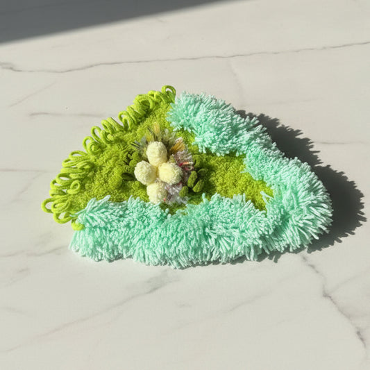 Jade Thicket handmade crochet moss coaster front view showing mint green and lime layered texture with white pompom flower cluster on marble surface – Sylva Garden