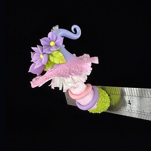 Handmade mauve curl fairy mushroom resin clay magnet with pink ruffled cap purple spiral stem and moss base, angled view with ruler on black background – Sylva Garden