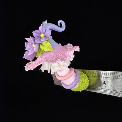 Handmade mauve curl fairy mushroom resin clay magnet with pink ruffled cap purple spiral stem and moss base, angled view with ruler on black background – Sylva Garden