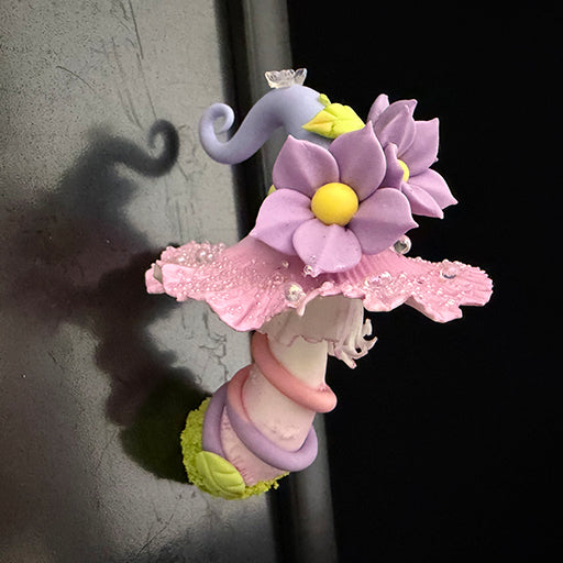 Handmade mauve curl fairy mushroom resin clay magnet with purple flowers and pink ruffled cap attached to metal refrigerator door, lifestyle view – Sylva Garden