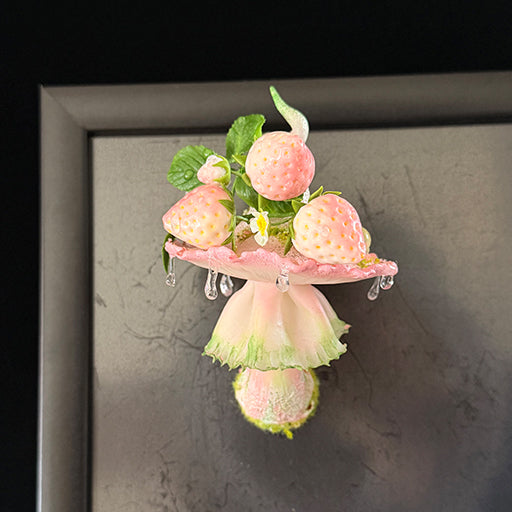 Handmade milky spore strawberry mushroom resin clay magnet with pink ruffled cap and strawberry accents attached to grey metal frame, lifestyle view – Sylva Garden