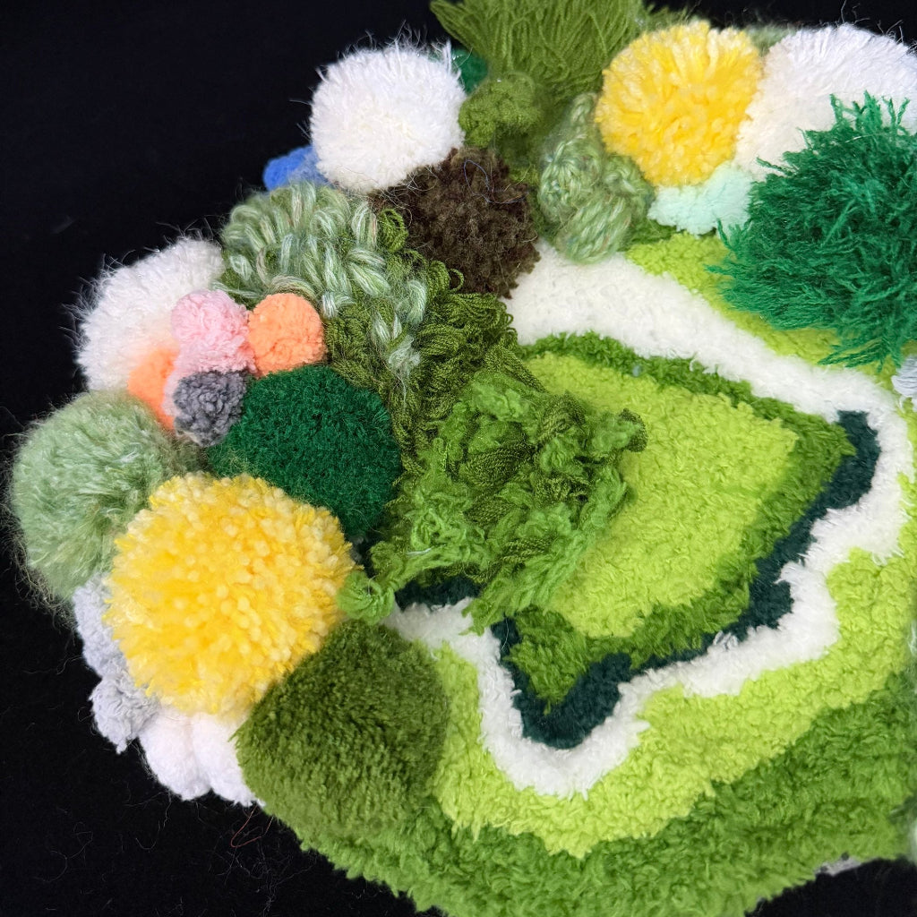 Handmade Moss Wanderer green multi-texture pom-pom crochet coaster close-up detail showing mixed green yellow orange and pink pom-pom textures with white wavy center border on black background – Sylva Garden
