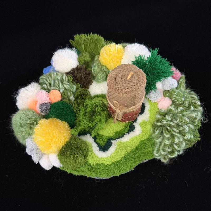 Handmade Moss Wanderer green multi-texture pom-pom crochet coaster styled with beeswax pillar candle on black background, angled side lifestyle view – Sylva Garden