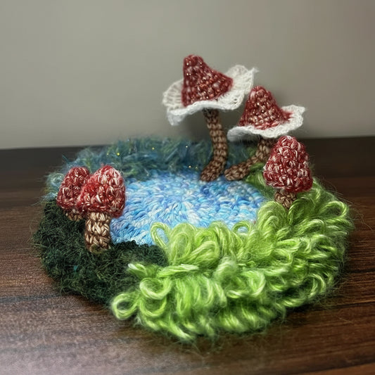 Handmade Pixie Ring red lace mushroom crochet moss coaster with blue center and curly green moss border, side view on wooden table – Sylva Garden