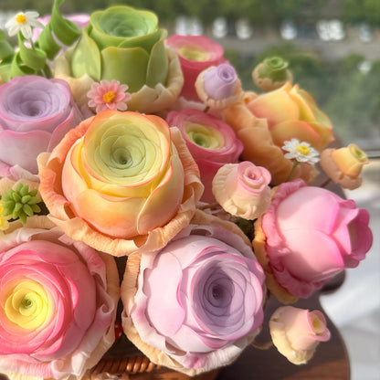 Rose Succulent Carnival handmade clay arrangement side view by window showing orange pink and purple ranunculus blooms with green succulent rosettes and white daisy in woven basket – Sylva Garden