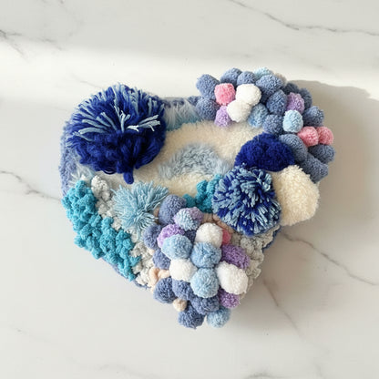Handmade Tidal Moss blue white gradient pom-pom crochet coaster with navy sky blue lavender and cream pom-poms, angled side view on white marble surface – Sylva Garden