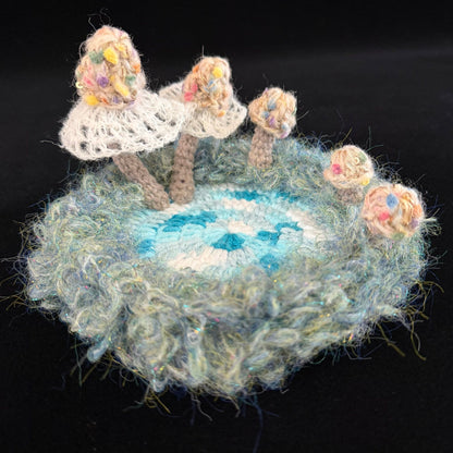 Handmade Whisper Cap ivory lace mushroom crochet moss coaster angled side view showing white lace veil mushrooms teal blue center and fluffy moss border on black background – Sylva Garden