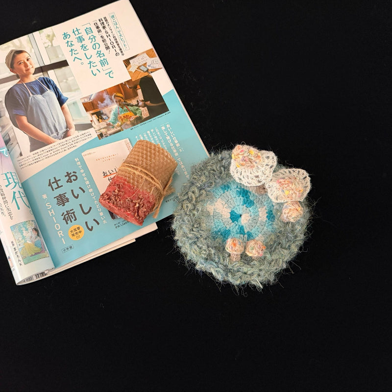 Handmade Whisper Cap ivory lace mushroom crochet moss coaster styled with Japanese magazine and woven accessory on black background, lifestyle view – Sylva Garden